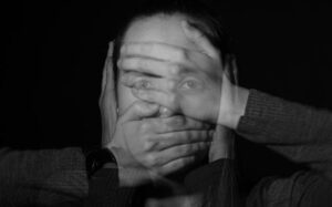 A black and white photo of a woman with several hands covering her eyes, mouth, and ears.
