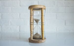 A clear hourglass with trickling sand has its simple wooden frame bound in wire.