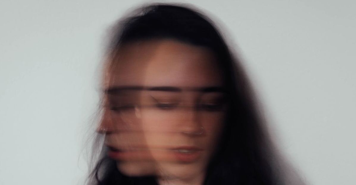 A blurred photo of a long-haired woman who seems to be shaking her head from side to side with her eyes closed.