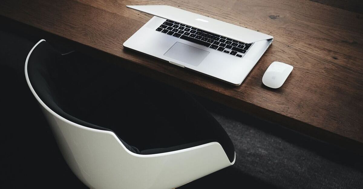 An artistic photo of a wireless mouse and laptop left partially closed and an office chair left askew. It looks like an employee has just got up and left their workstation.