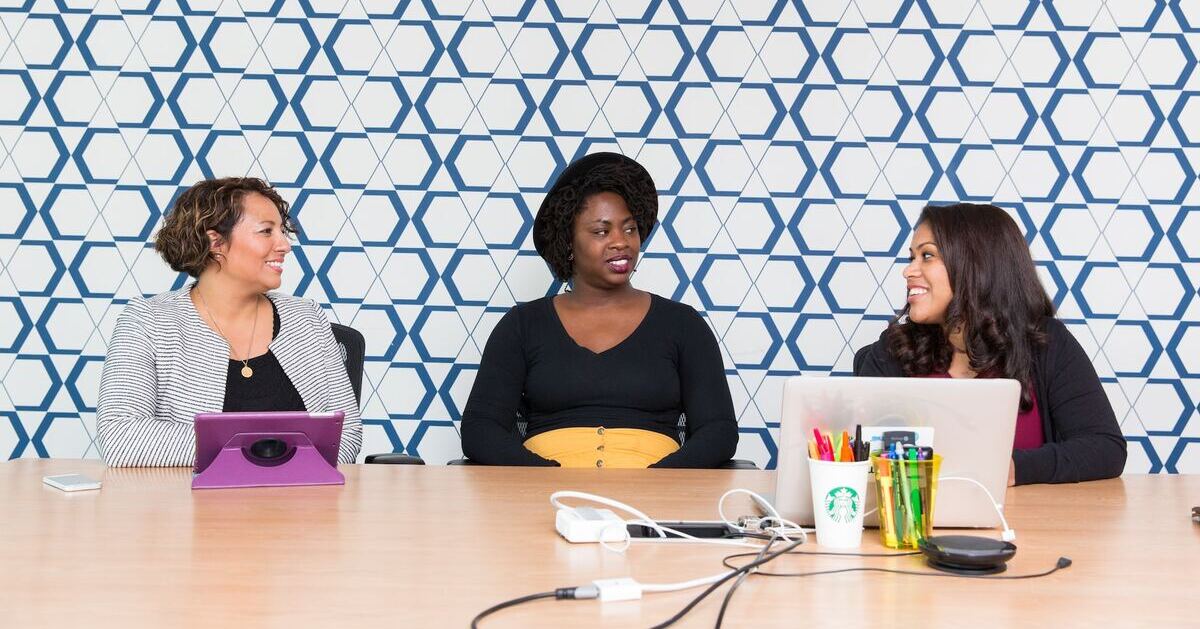 Three women discussing work in front of their laptops, with the boss in the middle listening intently.