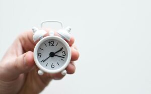 A hand holding a tiny white alarm clock.